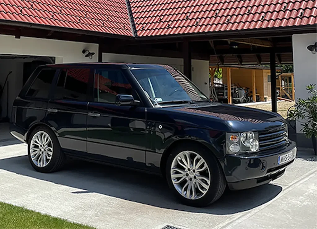Egy szép SUV parkol a ház előtt, fekete színű, csillog a napsütésben